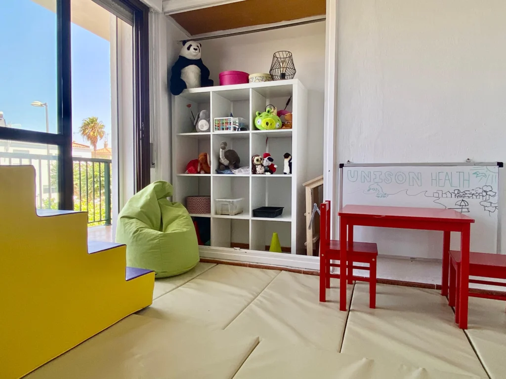 Children’s therapy room at Unison Health with toy shelves, a small red table and a whiteboard