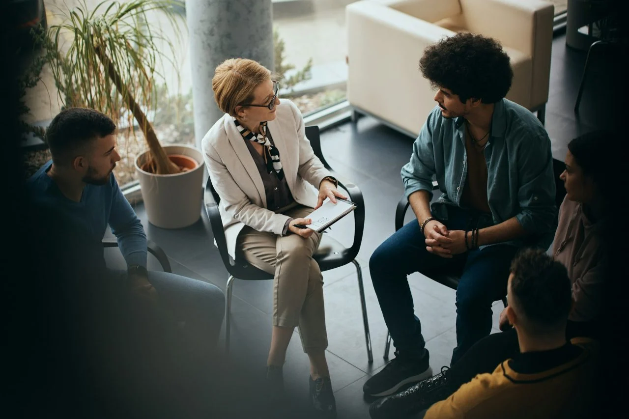 Group therapy session with adults sitting in a circle around a counselor
